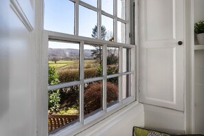 Une fenêtre donnant sur un jardin et sur des collines lointaines.