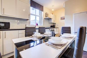 A modern kitchen with white cabinets, a dining table set for four, and a window providing natural light. - Perfect Booking Deptford High Street 3 Bed Flat (London)