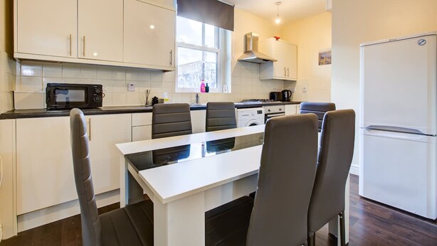 A modern kitchen with white cabinets, a dining table with chairs, a microwave, a stove, and a refrigerator. - Perfect Booking Deptford High Street 3 Bed Flat (London)