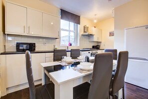 A modern kitchen with white cabinets, a dining table with chairs, a microwave, and a refrigerator. - Perfect Booking Deptford High Street 3 Bed Flat (London)