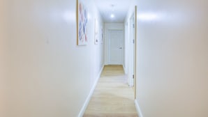 A narrow hallway with a wooden floor, white walls, and a door at the end. - Perfect Booking Deptford High Street 3 Bed Flat (London)