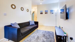 A modern living room with a dark sofa, a grey rug, wall-mounted decor, and a TV. - Perfect Booking Deptford High Street 3 Bed Flat (London)