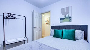 A bedroom with a bed, a hanging clothes rack, a door, and a wall with a painting. - Perfect Booking Deptford High Street 3 Bed Flat (London)