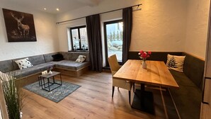 En moderne stue med en sofa, et træbord, et lille sofabord og udsigt til et sneklædt landskab gennem et vindue.