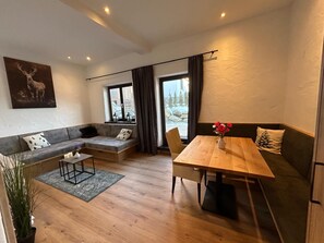 Ein modernes Wohnzimmer mit einer Couch, einem Holzesstisch, einem kleinen Couchtisch und Blick auf eine verschneite Landschaft durch ein Fenster.
