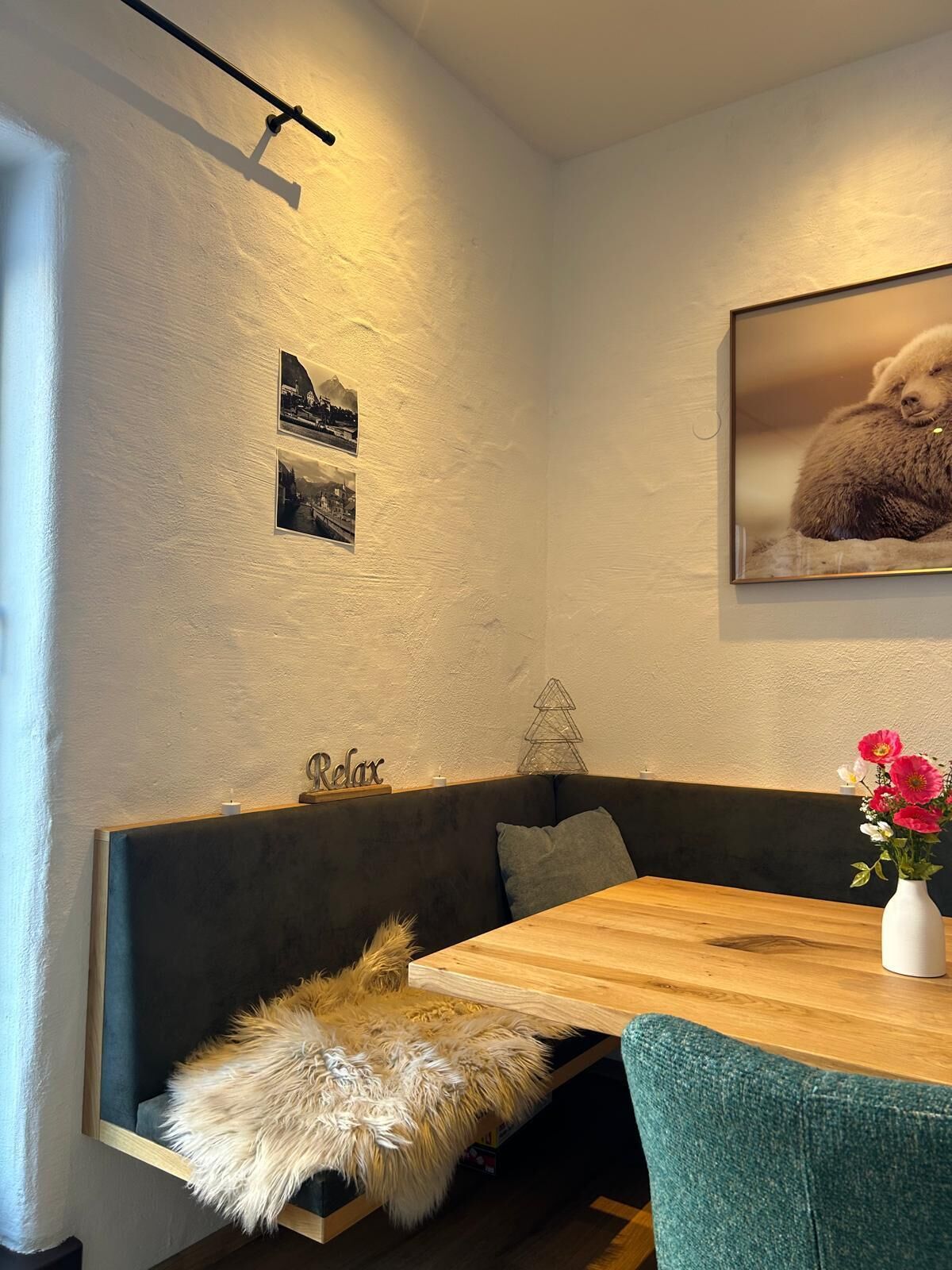 Una habitación acogedora con una mesa de madera, un sofá verde oscuro, un cojín blanco mullido, un cuadro colgado en la pared de un oso y un letrero que dice 'Relax'.