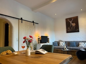 Ein modernes Wohnzimmer mit einem Holzesstisch, einer Couch, einem Fernseher und einem Bild eines Rehs.