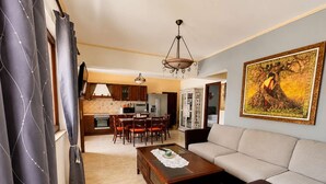 A living room with a sofa, a coffee table, and a dining area with chairs and a table. - Sunny Retreat - Kefalos Stay with Patio & Parking (Kamari)