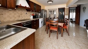A kitchen with granite countertops, wooden cabinets, a built-in oven, and a dining area with a table and chairs. - Sunny Retreat - Kefalos Stay with Patio & Parking (Kamari)