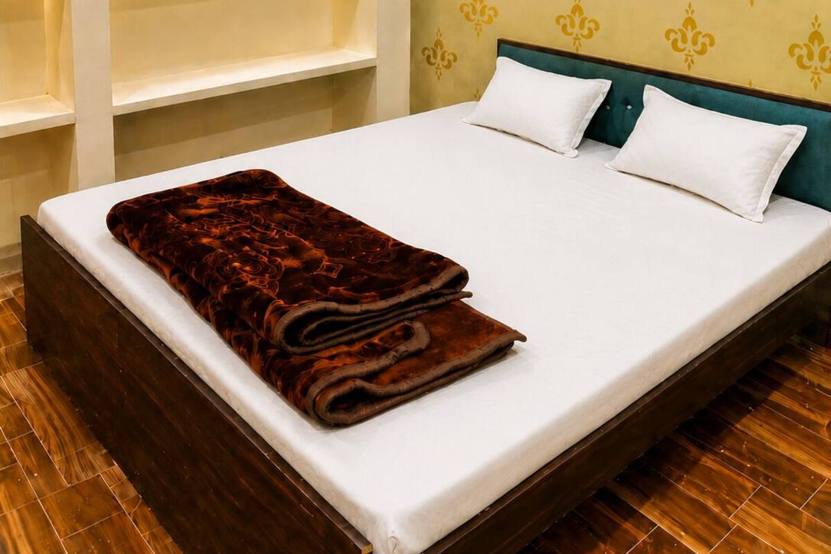 A hotel room with a bed, white pillows, a brown blanket, a ceiling fan, and an air conditioning unit.