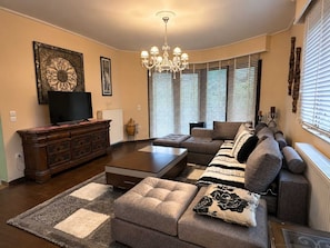 A living room with a sofa, ottoman, coffee table, TV, and decorative items. - Peaceful Retreat - Kefalos Stay with Patio & Views (Καμάρι)