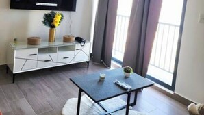 Ein Wohnzimmer mit Flachbildfernseher, Couchtisch, Sofa und Balkon mit Vorhängen.