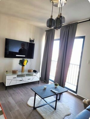 Ein Wohnzimmer mit Flachbildfernseher, Couchtisch, Sofa und Balkon mit Vorhängen.