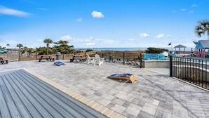 Una terraza de madera con mobiliario exterior, vistas a la playa y un pabellón.