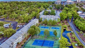 Vista aérea de una zona residencial con varias canchas de tenis, una piscina y una carretera que serpentea por la propiedad.