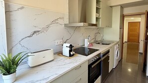 A modern kitchen with a marble backsplash, stainless steel appliances, and a built-in oven. - Dragos Suites 105 (Arrecife)
