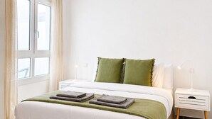 A neatly arranged bedroom with a bed, bedside tables, a lamp, and a window with curtains. - Dragos Suites 105 (Arrecife)
