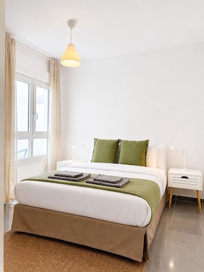 Ein ordentlich eingerichtetes Schlafzimmer mit einem Bett, Nachttischen, einer Lampe und einem Fenster mit Vorhängen.