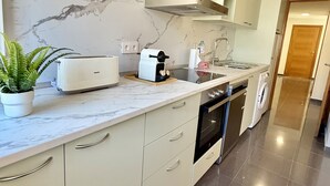 A modern kitchen with a marble backsplash, a built-in oven, a dishwasher, and a countertop with a toaster and a plant. - Dragos Suites 105 (Arrecife)