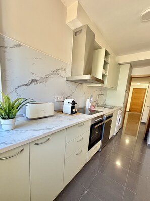 Eine moderne Küche mit Marmor-Spritzschutz, einem Einbauofen, einem Geschirrspüler und einer Arbeitsplatte mit Toaster und Pflanze.