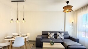 A modern living room with a sofa, coffee table, dining area, and pendant lighting. - Dragos Suites 105 (Arrecife)