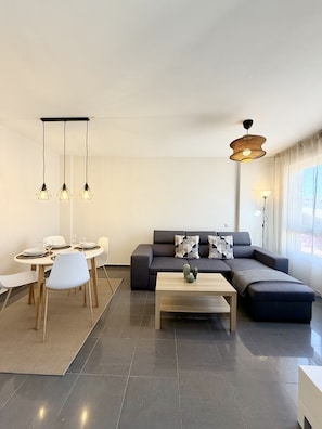 Ein modernes Wohnzimmer mit Sofa, Couchtisch, Essbereich und Pendelleuchten.