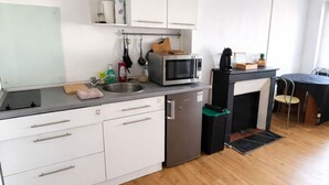 Ett kompakt kök med vita skåp, en mikrovågsugn, en diskho och ett litet kylskåp.