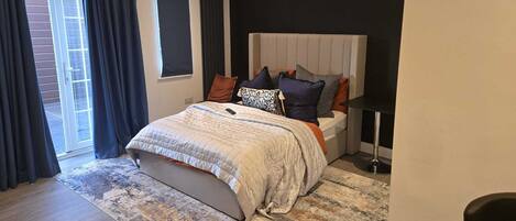 A modern bedroom with a large bed, a bedside table, a chair, a floor lamp, and a view of the outside.