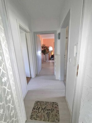 A hallway with a welcome mat, white walls, and a door leading to another room.