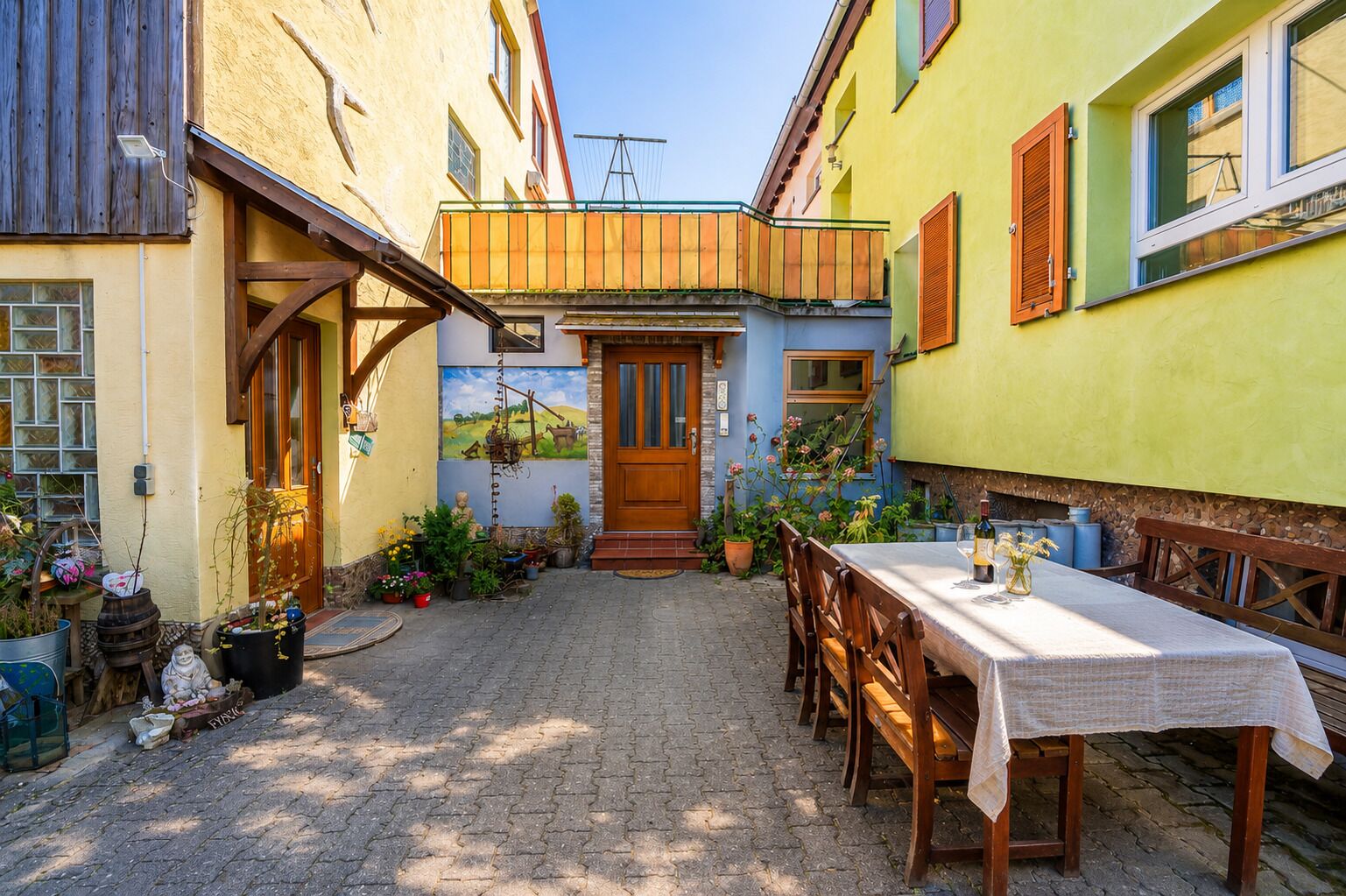 A courtyard with a wooden table and chairs, surrounded by colorful buildings with a door and windows.