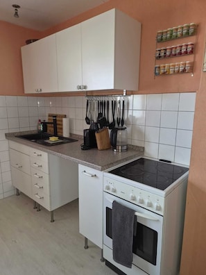 Une cuisine avec des meubles blancs, une cuisinière, un évier et un porte-épices.