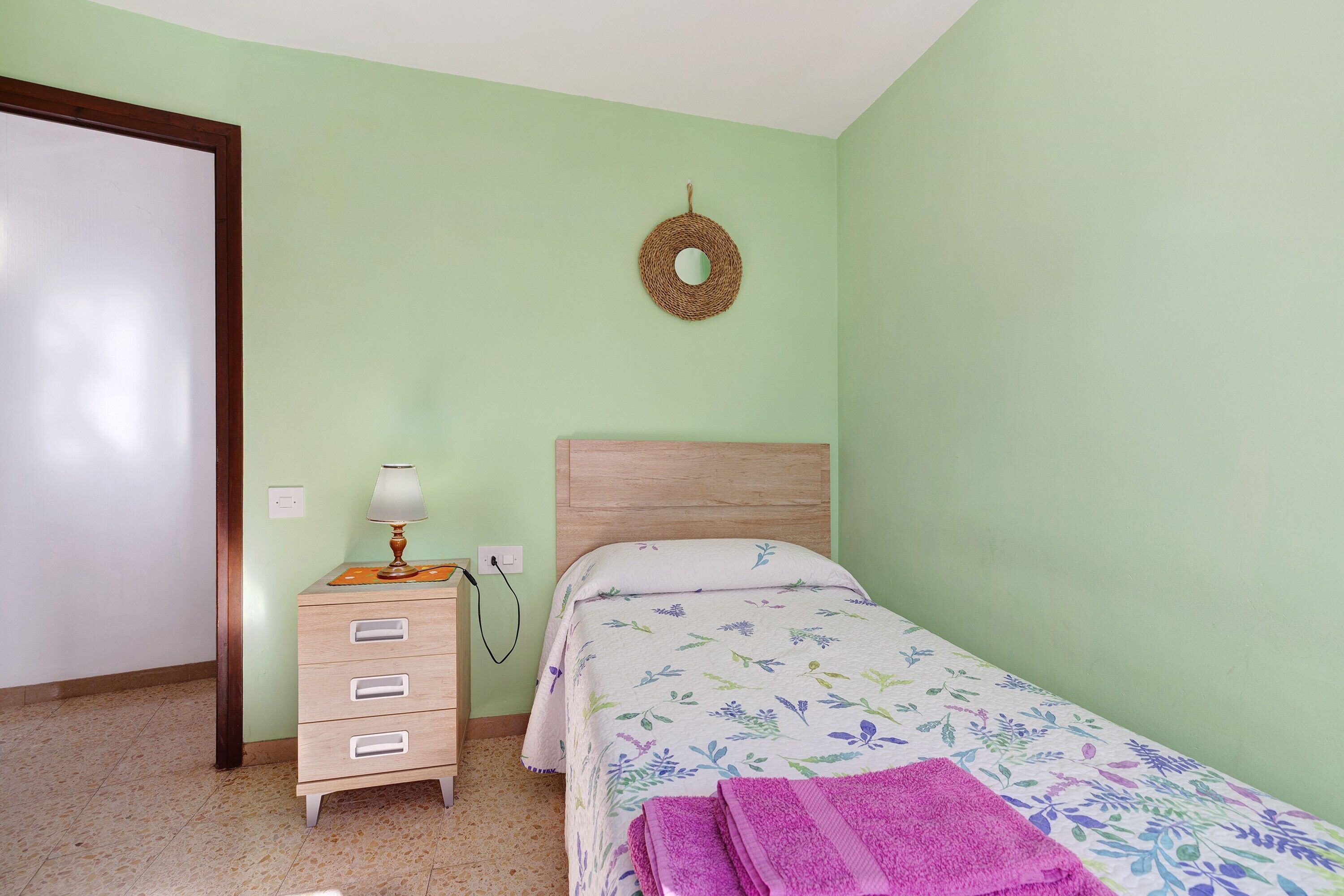 A bedroom with a bed, a dresser, a lamp, and a wall-mounted decoration.