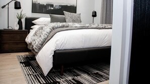 Une chambre moderne comprenant un lit, des tables de chevet, une commode, une lampe sur pied, une œuvre d’art accrochée au mur et une fenêtre avec des rideaux.