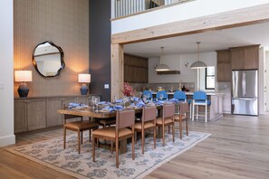 Un coin repas avec une table en bois dressée pour six personnes, entourée de chaises, dans une cuisine moderne dotée de meubles en bois et d’un grand réfrigérateur.