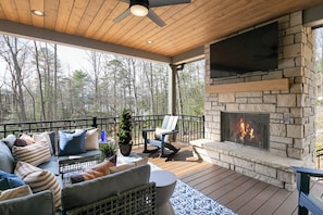 Une terrasse couverte avec une cheminée en pierre, des sièges d’extérieur et une vue sur la forêt environnante.