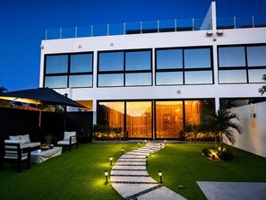 A modern two-story building with a glass facade, a paved pathway leading to the entrance, and outdoor seating. - 3BR Villa w/ Rooftop Ocean View Terrace and Racquet Club Access | 5m to Beach (Noord)