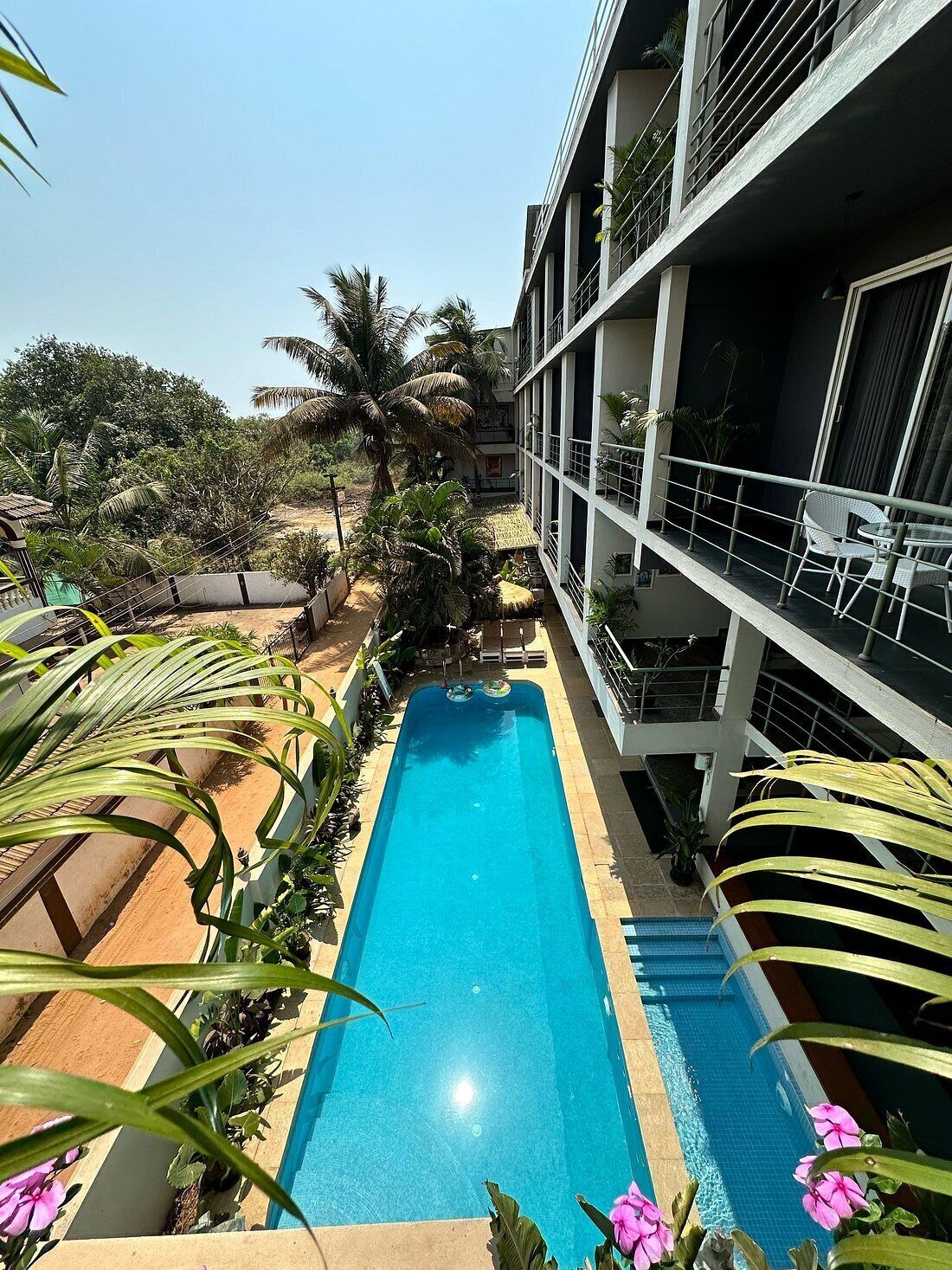 A hotel with a swimming pool, surrounded by greenery and palm trees.