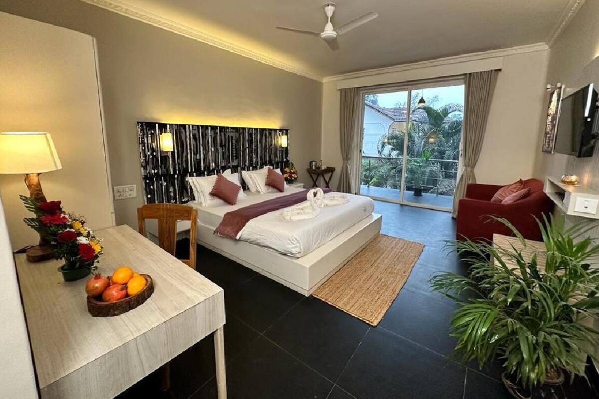 Una habitación de hotel moderna con cama, escritorio con lámpara, televisor, sofá rojo y balcón con vistas.