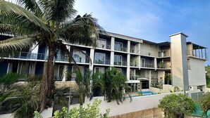 A multi-story hotel with balconies, a swimming pool, and tropical landscaping.