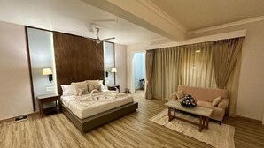 A hotel room with a bed, a sofa, a coffee table, a mirror, a ceiling fan, and curtains.