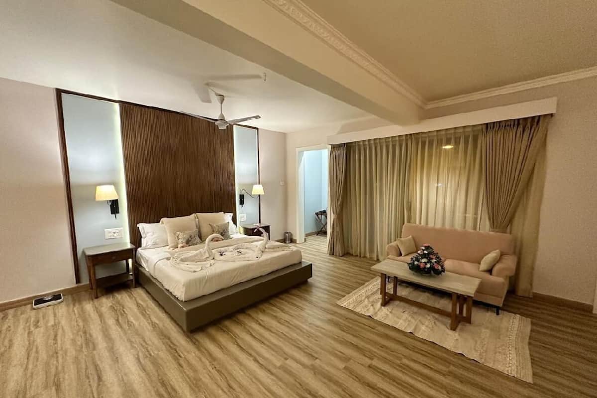 Habitación de hotel con cama, sofá, mesa de centro, espejo, ventilador de techo y cortinas.