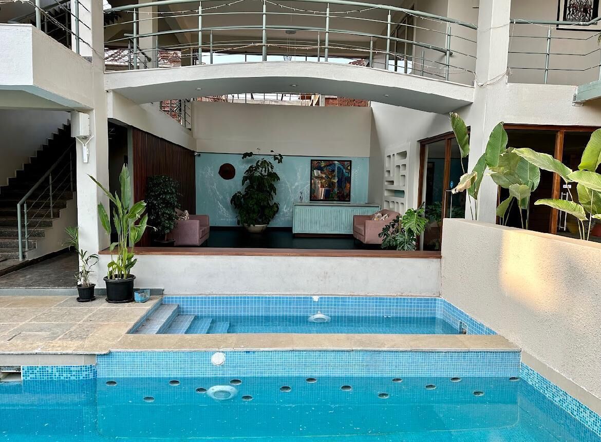 A swimming pool with steps leading into it, surrounded by potted plants and a balcony.