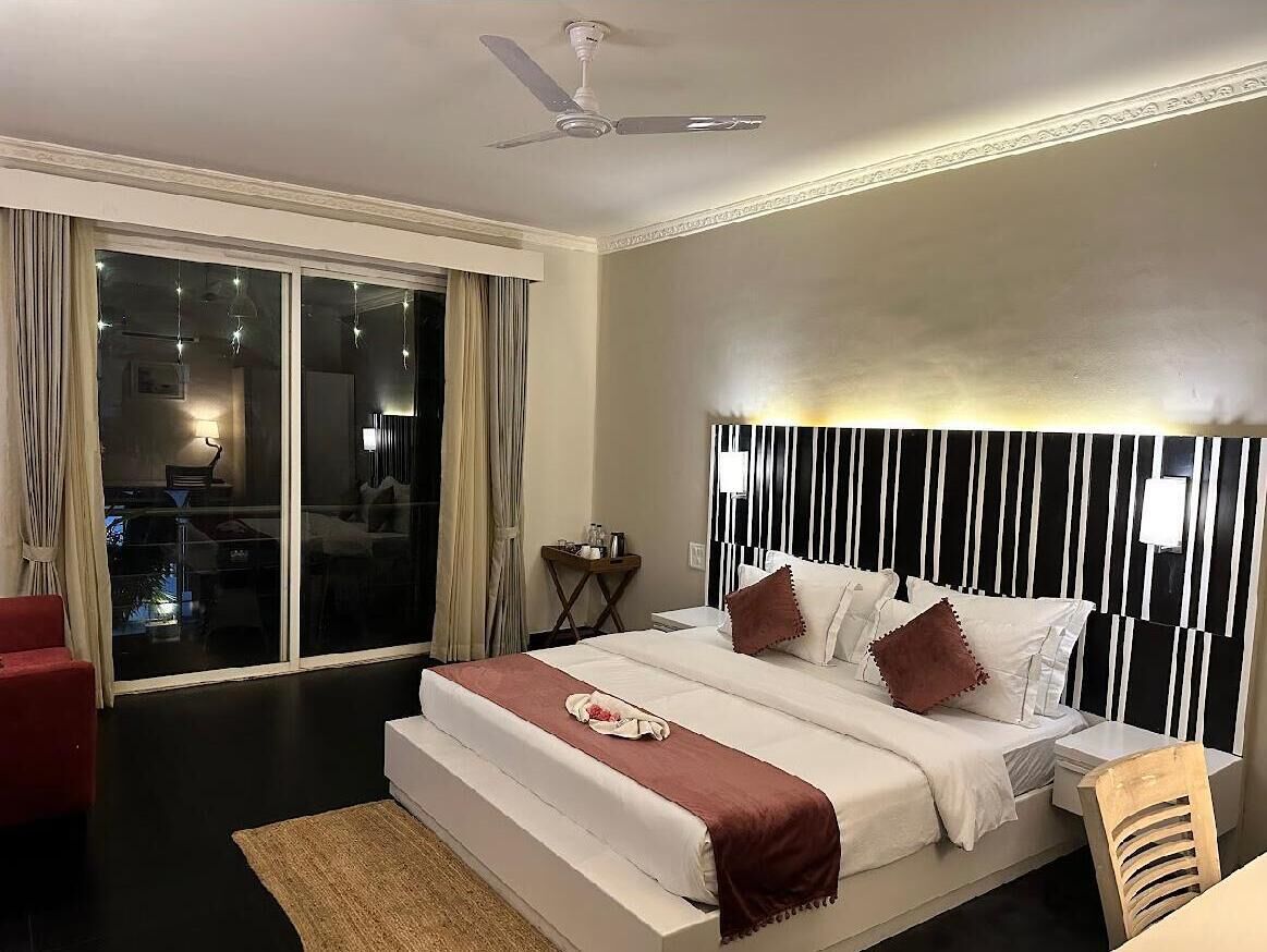 A hotel room with a bed, a ceiling fan, a nightstand, and a view through a sliding door.