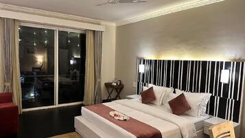 A hotel room with a bed, a ceiling fan, a nightstand, and a view through a sliding door.