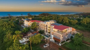 A multi-story building with a red roof, surrounded by lush greenery and overlooking a coastline.