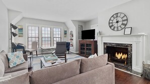 A living room with a fireplace, a clock, and a television. - Central-Immaculate-Parking-Fenced Yard-Dining (Fort Wayne)