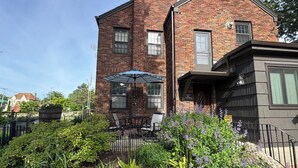 A brick building with a patio area, outdoor seating, and a garden with various plants and flowers. - Central-Immaculate-Parking-Fenced Yard-Dining (Fort Wayne)