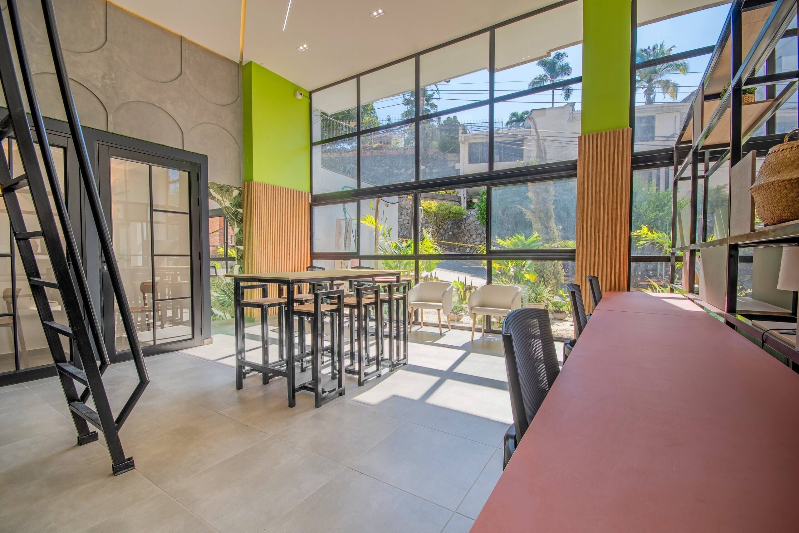A modern interior with a long table and chairs, large windows, and a view of the outdoors.