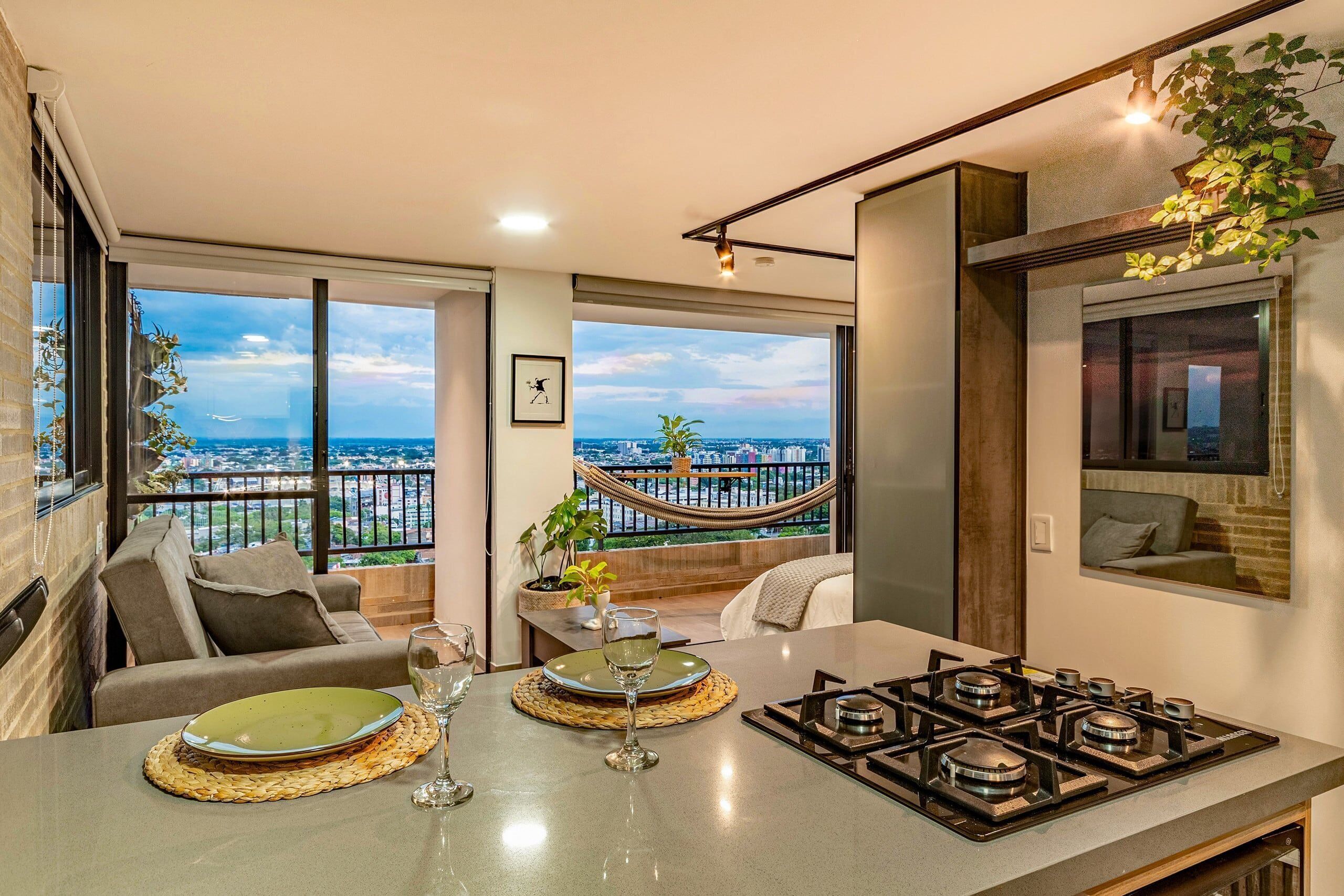 Una cocina moderna con vista a la ciudad, un área de comedor con sofá y un balcón con hamaca.