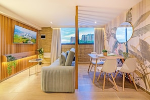 A modern living room with a sofa, dining table, chairs, a TV, and a large window with a city view. - Edificio Habitare Cristales (Cali)